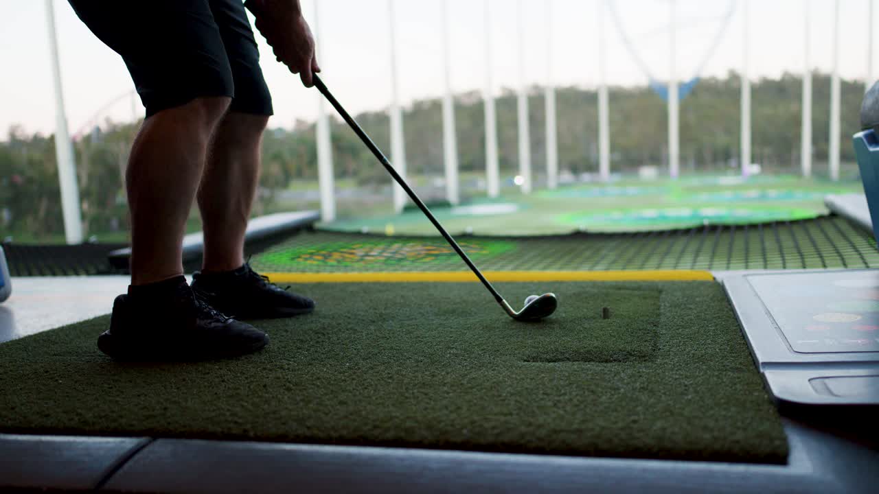 Person hits golf ball on driving range mat, side view, natural daylight, smooth camera movement