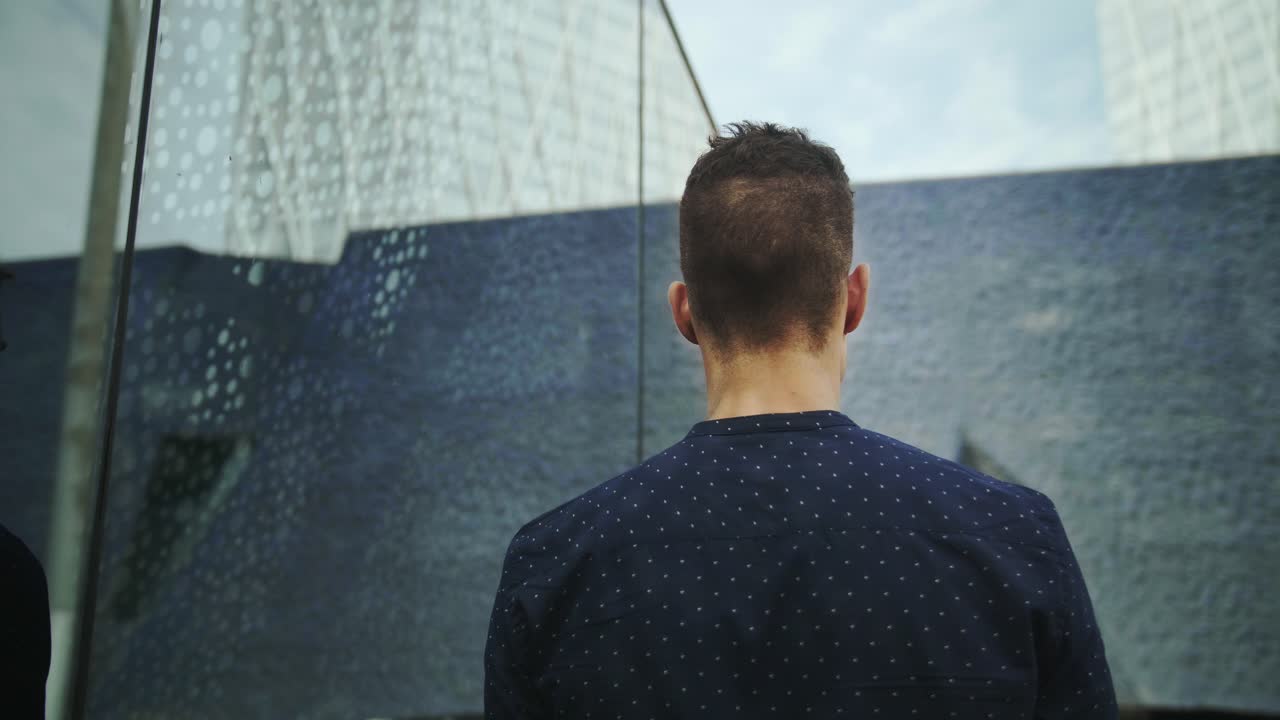 잘 차려입은 기업가 사업가 젊고 매력적인 트렌디한 남자가 현대적인 건물 창문에 비친 자신의 모습을 들여다본 다음 슬로우 모션으로 걸어갑니다
