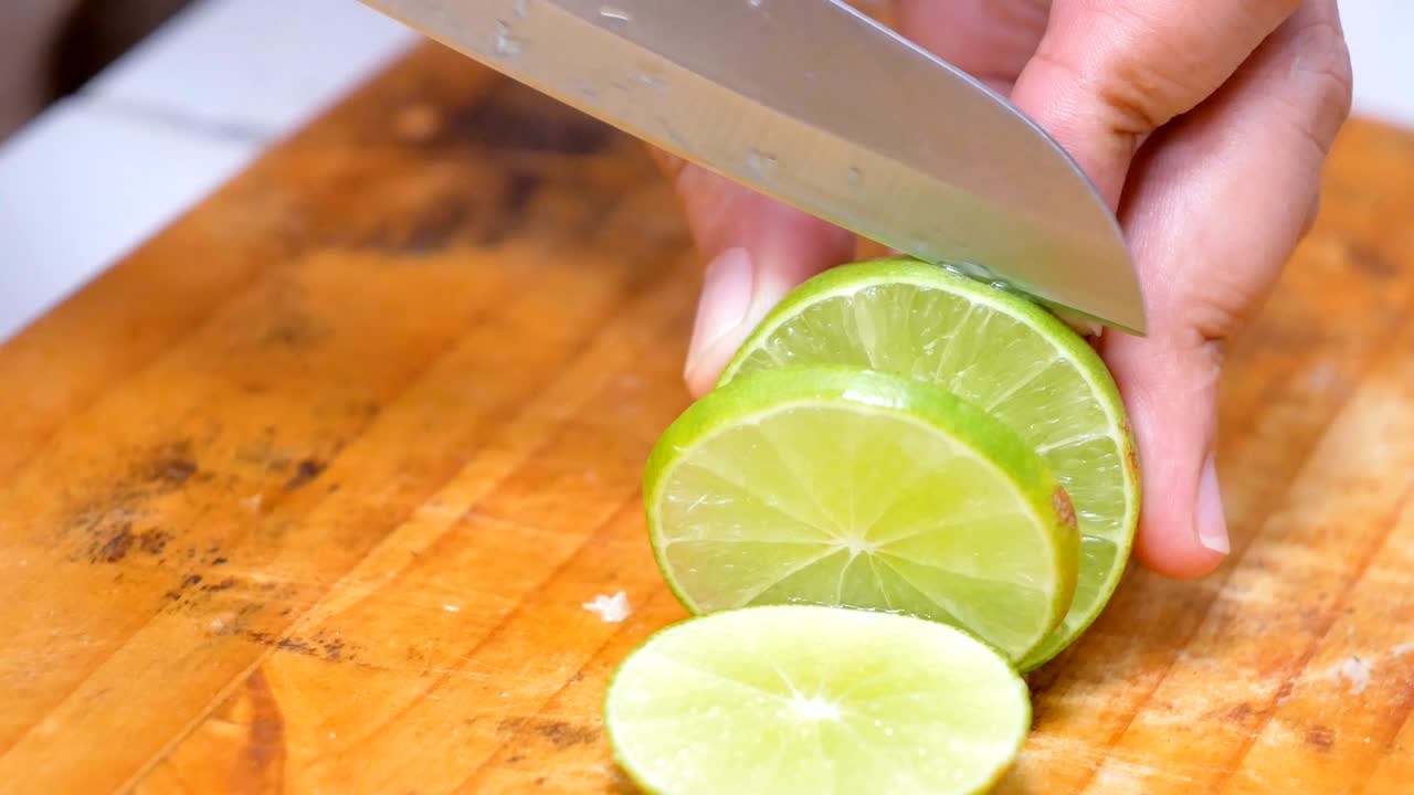 manos de mujeres usando un cuchillo cortaron la cal verde en pedazos en una tabla de madera en una cocina
