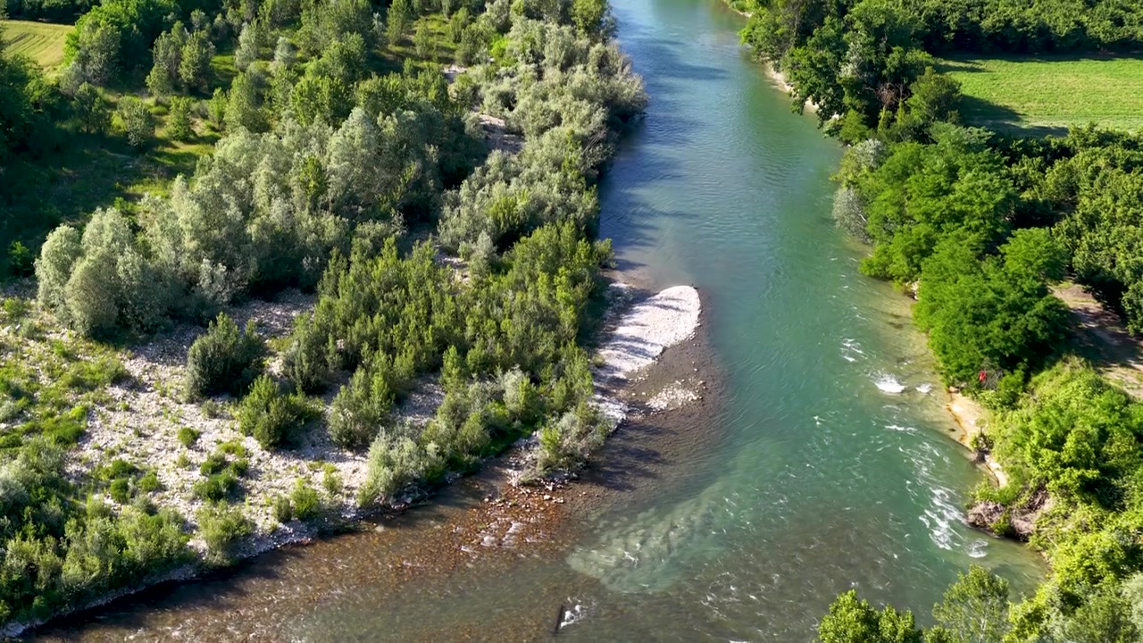 Záběr dronem z výšky na klikatou řeku s kamenitými břehy a bujnou zelenou vegetací.