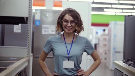 Positive-female-seller-or-shot-assistant-portrait-in-supermarket-store.-Woman-in-blue-shirt-and-empty-badge-looking-at-the