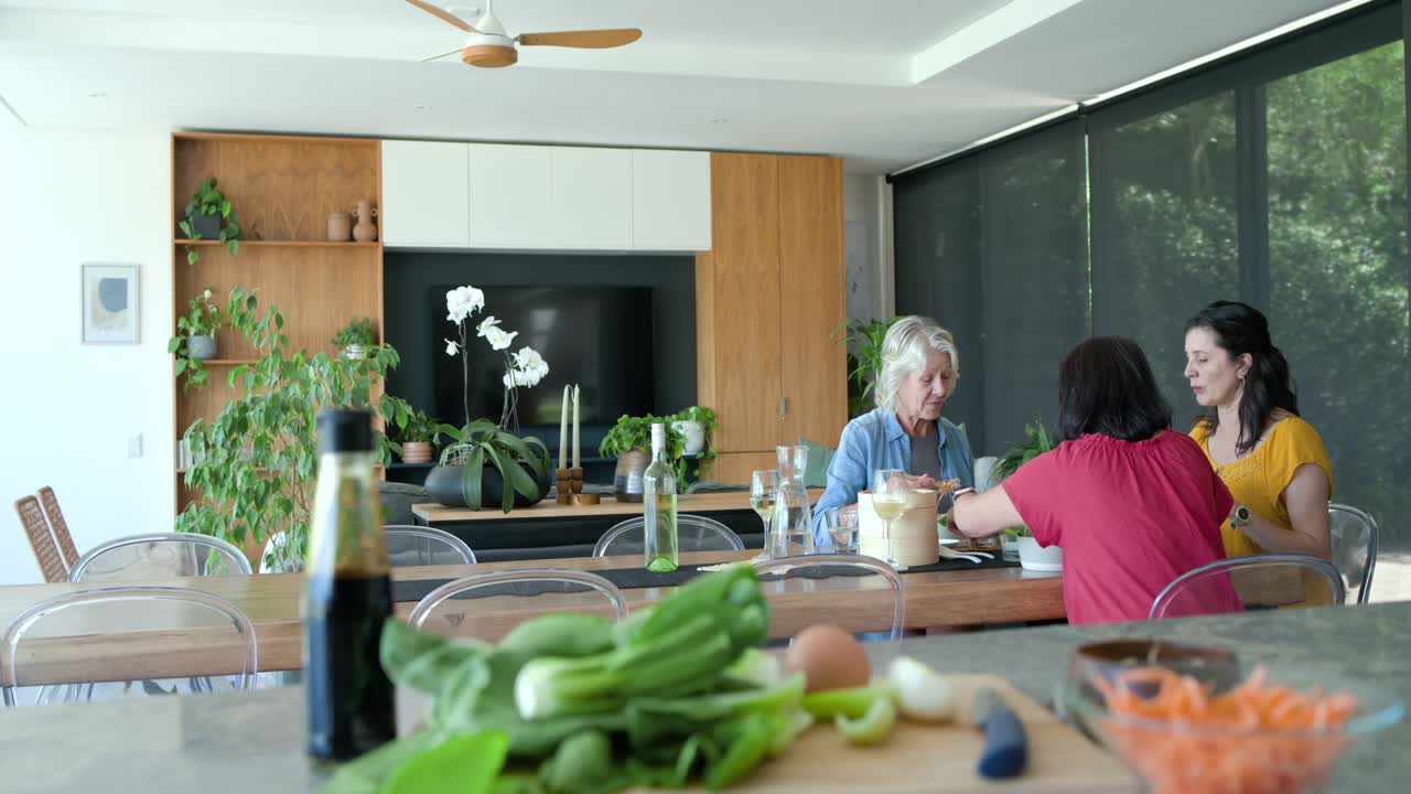 Mulheres da família com uma idosa provando um prato após um aviso do telefone para experimentar uma receita na mesa da cozinha.