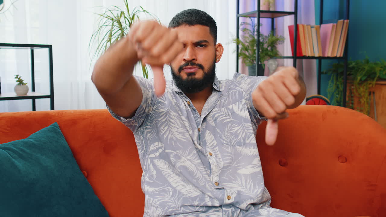 Upset arabian man showing thumbs down dislike bad work disapproval dissatisfied feedback at home