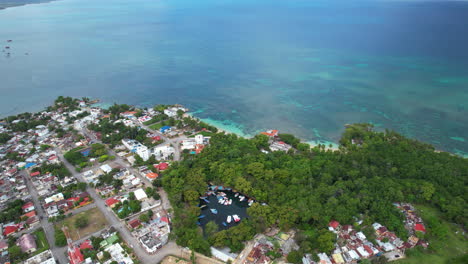 anchored boats in port lake surrounded by mangrove in rio san juan town. caribbean sea and coastline in background. aerial tilt up shot