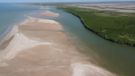 slow moving drone shot of creek joining ocean past a sandy beach in darwin, northern territory