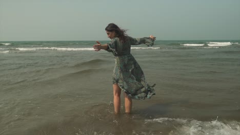 girl with flowing long dress slowly turning with waves breaking around her