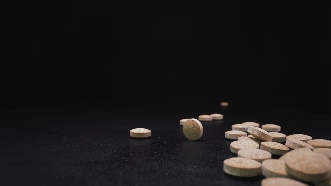 arrojando pequeñas píldoras de drogas beige para apilar en la superficie negra