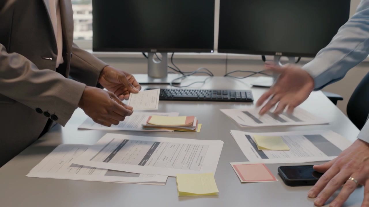 Pointing blazer-clad woman and shirt-clad man handing card on office table after reports for review