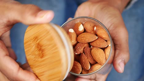 manos sosteniendo un recipiente de madera con tapa y un cuenco de almendras