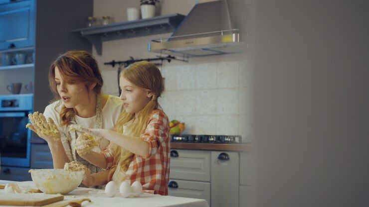 Happy mother and daughter kneading a daugh for muffins or cookies together in the evening time in the modern nice kitchen. Indoors
