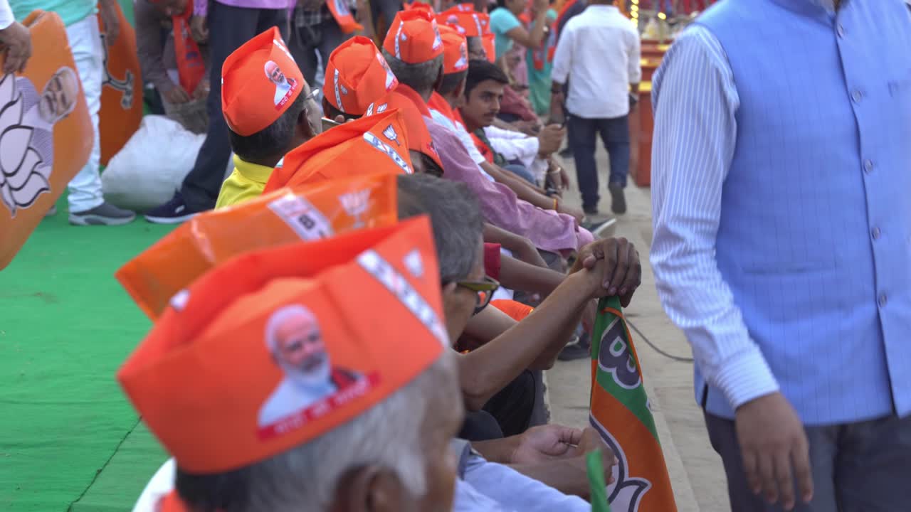 Group of Indian elderly people sitting in row wearing BJP merchandise to support Chief Minister Yogi Adityanath Lok Sabha election campaign rally
