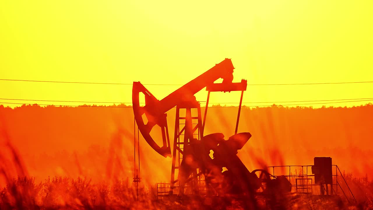 silueta de bombas de petróleo en un gran campo petrolífero al amanecer.