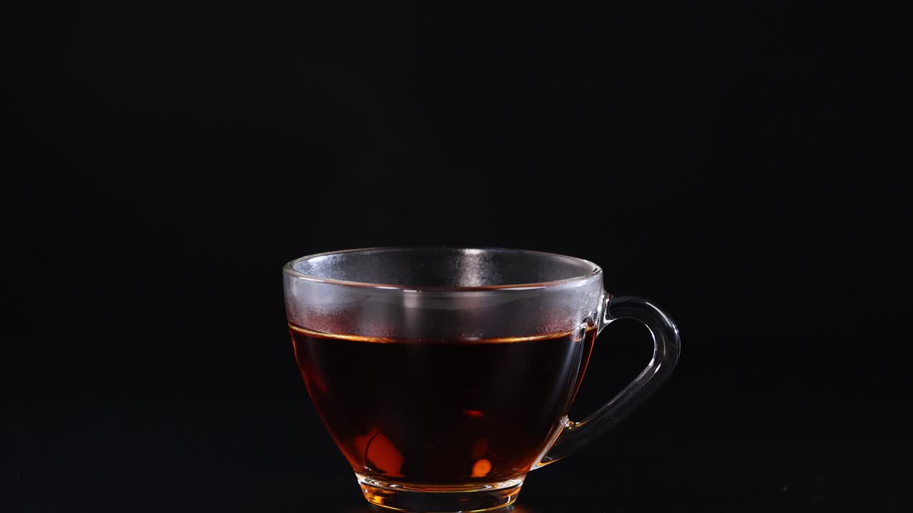 A sugar cube drops into a tea cup, creating a splash against a black background. Captured in high-speed photography