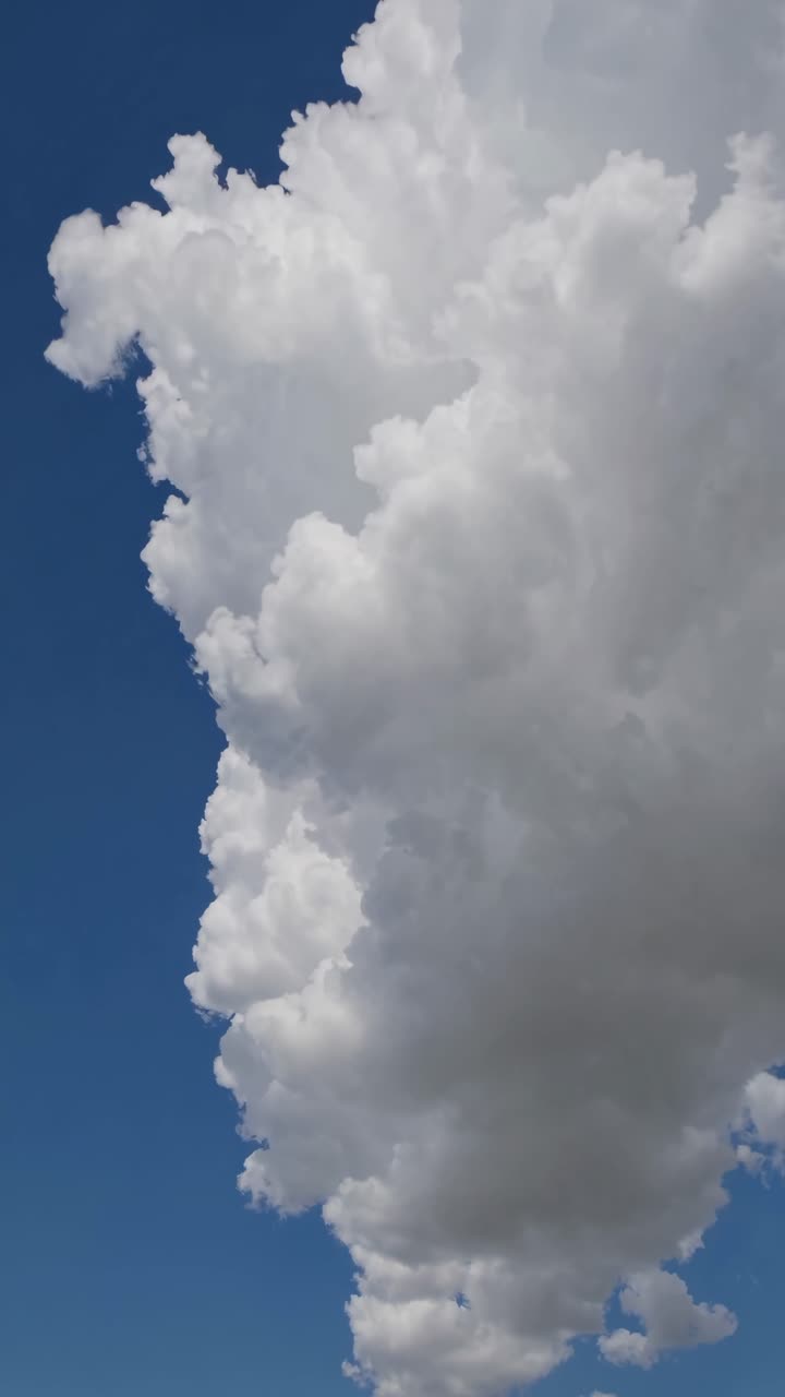 A low-angle shot of a towering cumulus cloud against a clear blue sky, capturing the cloud's