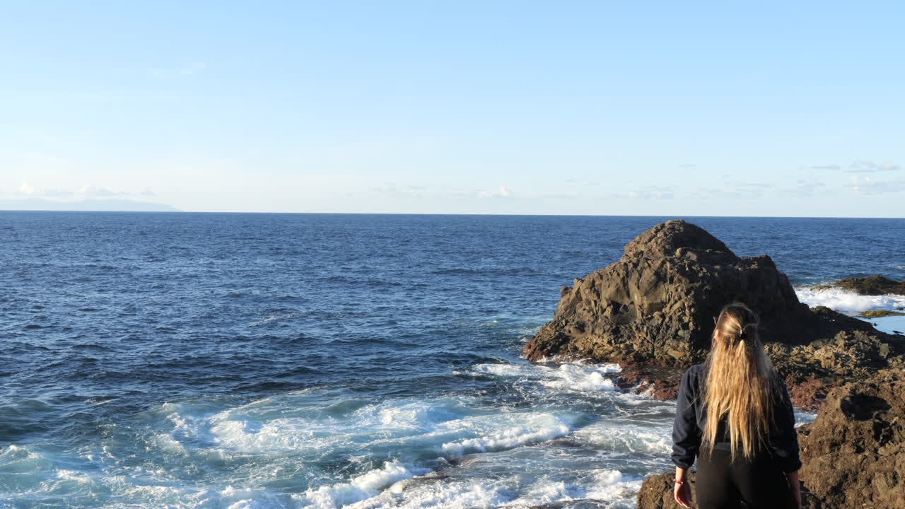 Shot of a woman who admires the waves of the sea and which are found on the coast of the municipality of Galdar, on the island of Gran Canaria and during sunset