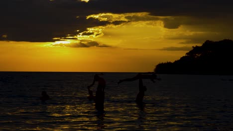 silhouettes of family playing in the sea with the sun setting in the background