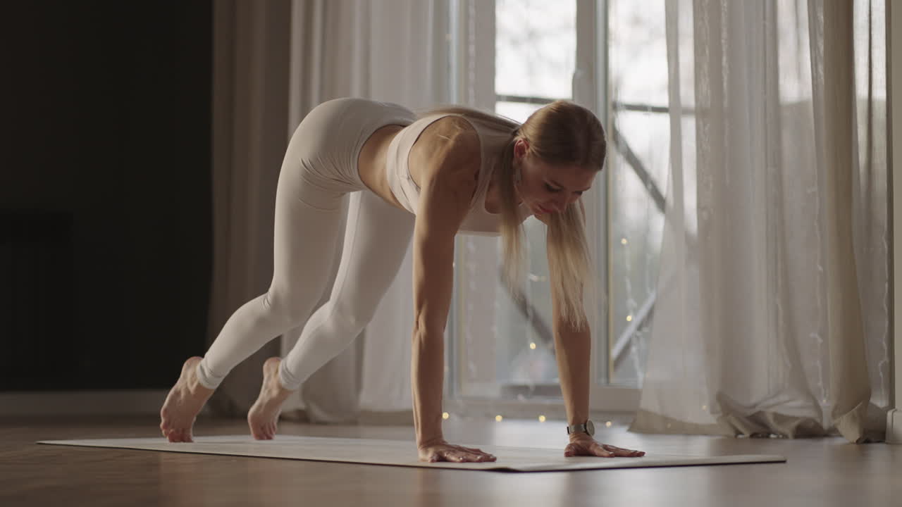 A young woman in white sportswear is stretching with a large hall with large windows in a slow-motion scheme the sun's rays shine through the window. Healthy lifestyle healthy morning
