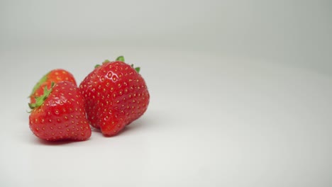 Drei-Köstliche-Rote-Erdbeeren,-Die-Sich-Auf-Dem-Tisch-Mit-Rein-Weißem-Hintergrund-Drehen---Nahaufnahme