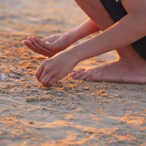 boy is playing on sand beach at sunset. boy making something with small pebbles on sand in the evening. happy childhood in summer time.