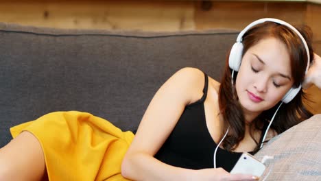 Woman-listening-to-music-on-mobile-phone-in-living-room