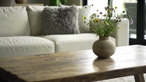 a cozy living room scene featuring a white sofa, textured throw pillow, and a rustic wooden coffee table adorned with fresh flowers in a neutral vase