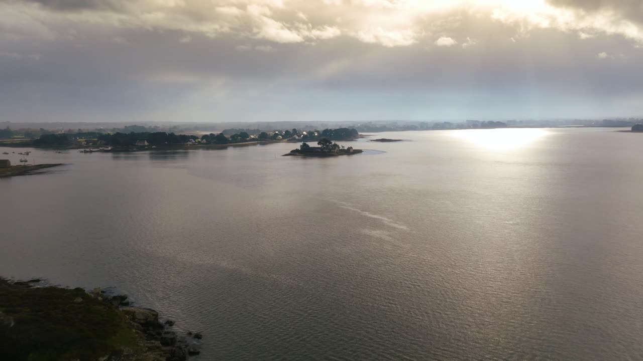 Veduta aerea cinematografica della luce solare che si riflette sull'acqua nel Golfo di Morbihan, Bretagna, Francia, con sagome di isole contro un cielo drammatico.