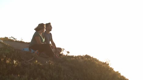 Couple-of-hikers-sitting-at-cliff-on-slope