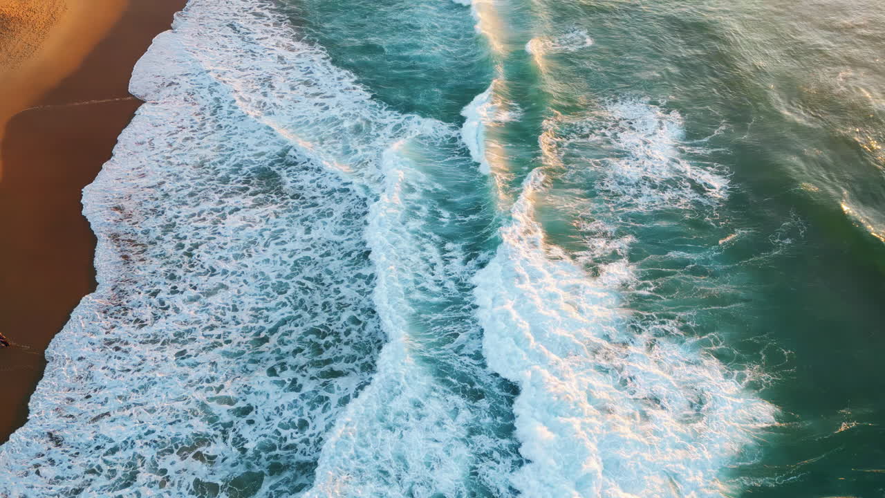 Drone view sandy beach with stunning stormy ocean at soft sunset sunlight.