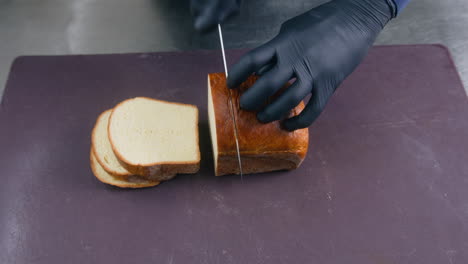 male cook cuts bread with knife on cutting board