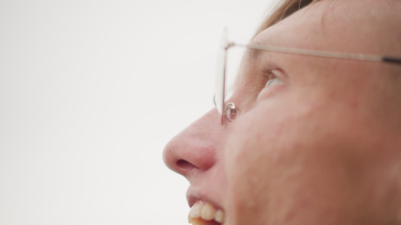 Primer plano de un hombre blanco con gafas, estudiante mirando hacia arriba con luz de estudio suave, expresión contemplativa, pecas sutiles, gafas de montura fina, fondo minimalista, ambiente tranquilo y esperanzador