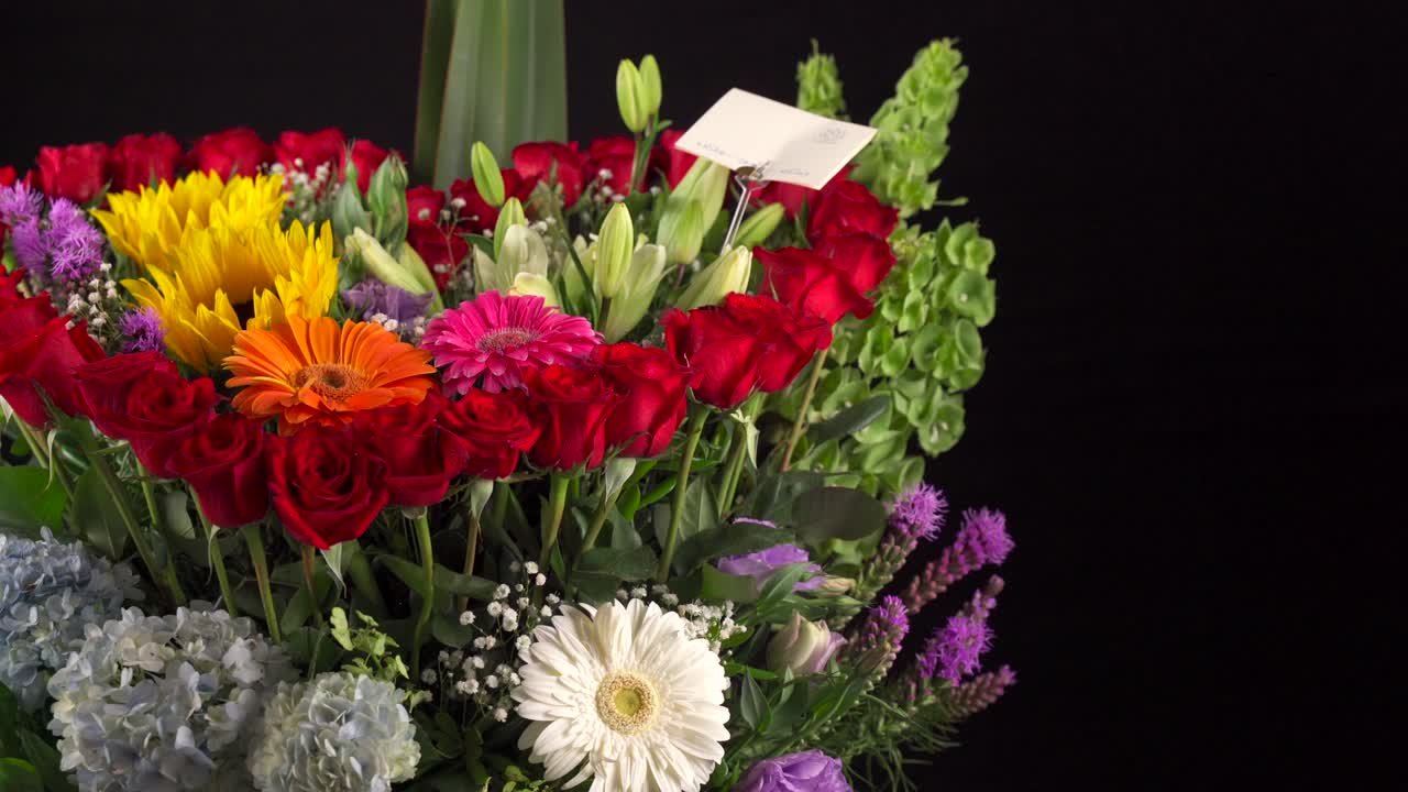 Composizione floreale d'amore a forma di cuore con girasoli, gerbere, margherite, gigli, gerbere, ripresa in slider su sfondo nero.
