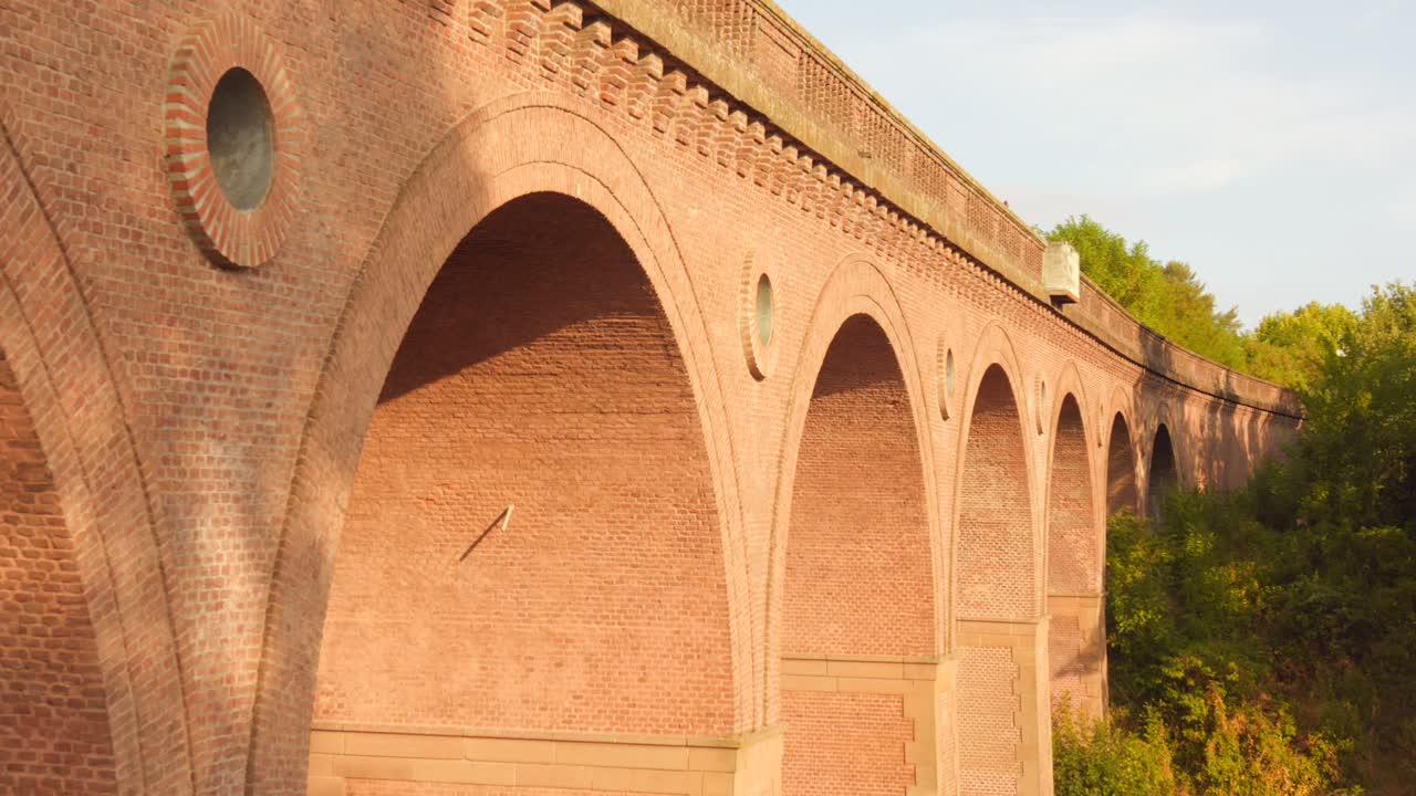 Massive red brick railway viaduct in Albi, France. Features a series of large arches and circular windows (oculi) in warm afternoon light