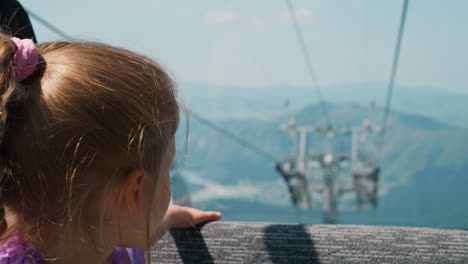 cute girl rides ropeway sitting on soft bench in gondola