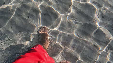 high angle personal perspective of male legs and feet and red swimwear walking in crystal clear shallow sea water