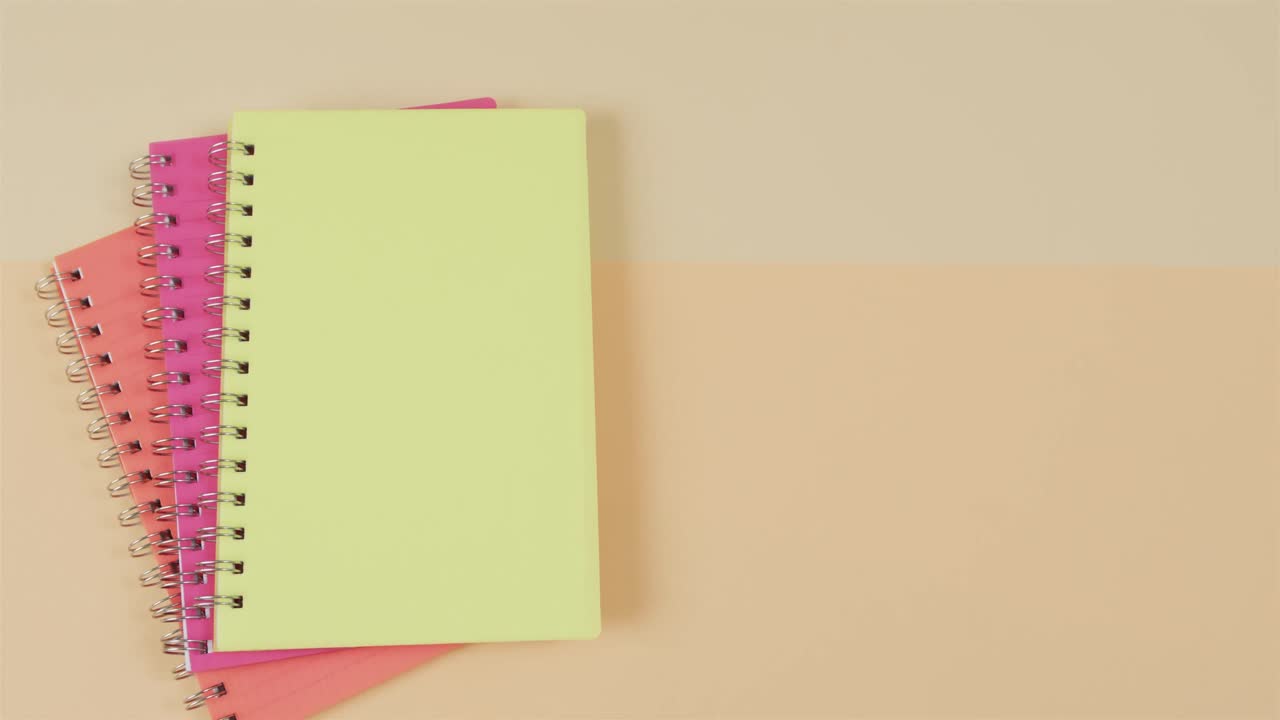 Overhead view of colourful notebooks with copy space on beige background, in slow motion