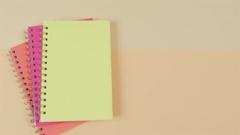 Overhead-view-of-colourful-notebooks-with-copy-space-on-beige-background,-in-slow-motion