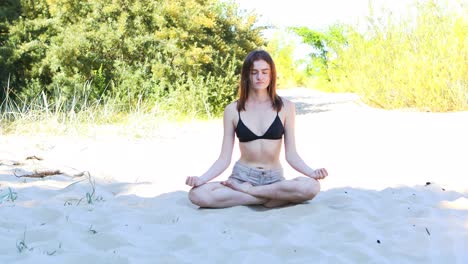 mujer joven sentada en una posición de loto en una playa, meditando a la sombra
