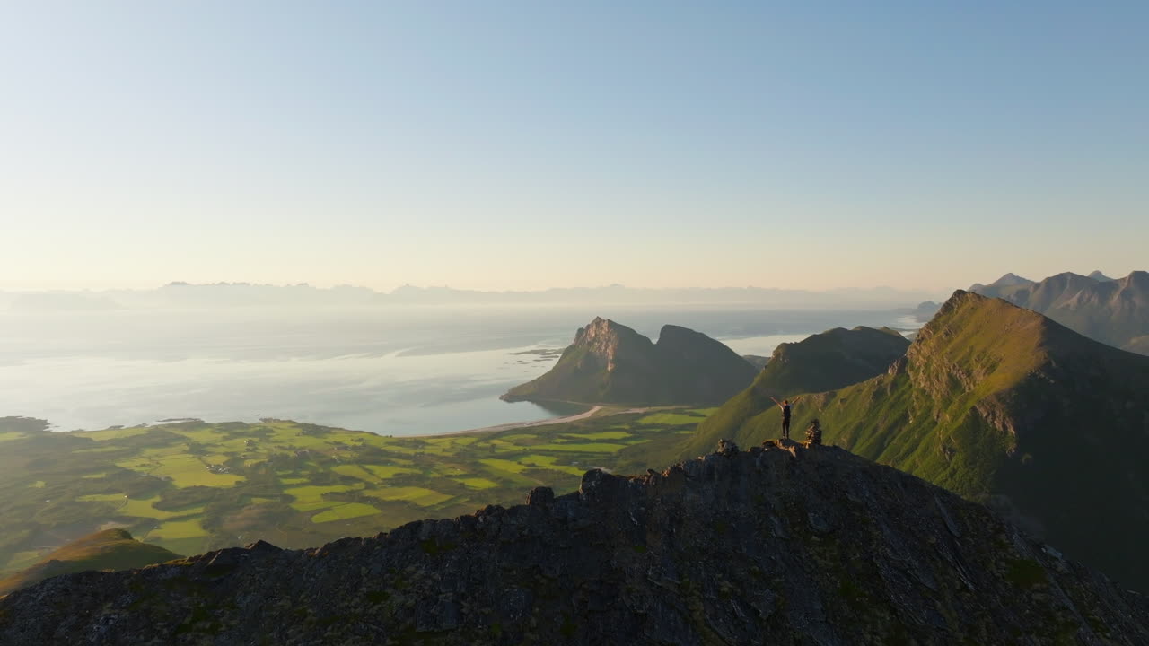 Man lift arms cheering on Norway mountain top with majestic coastal view