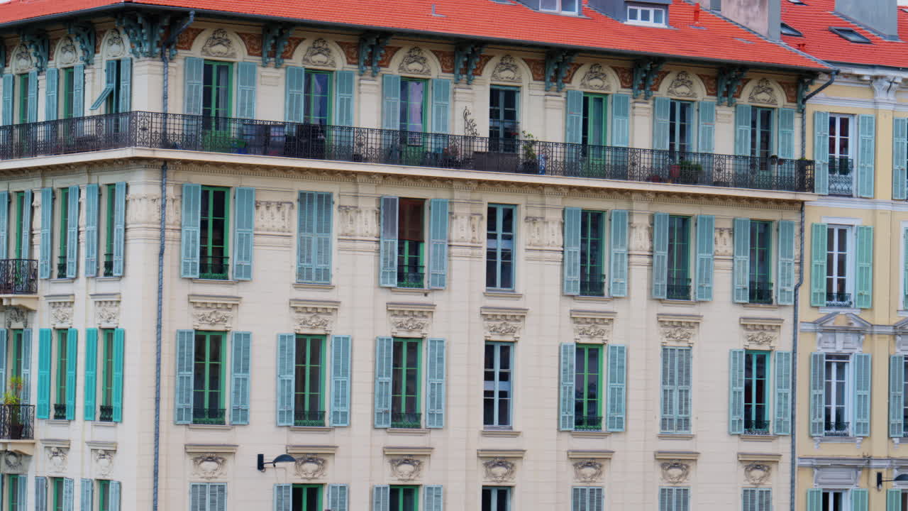 Multiple windows on the facade of a beige building with pastel turquoise shutters in Nice, France