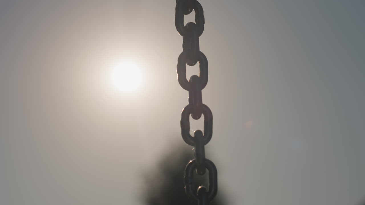 Vertical Chain Links Against Sun Hazy Tree Silhouette, Repeating Metal Pattern And Rust Texture, Minimalist Composition With Soft Flare And Quiet Atmosphere Evoking Age And Solitude
