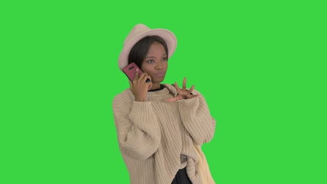 smiling african american woman in knitwear and hat talking on her phone on a green screen, chroma key