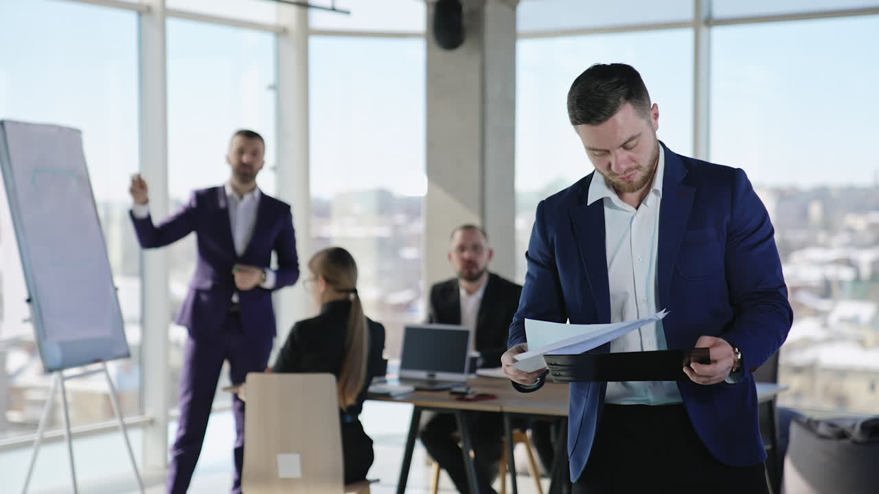 Young businessman looking through the business papers. Team of colleagues having business discussion at the table in the backdrop.