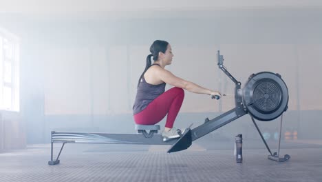 Mujer-Birracial-Determinada-E-Inalterada-Haciendo-Ejercicio-En-La-Máquina-De-Remo-En-El-Gimnasio,-En-Cámara-Lenta