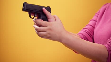 close up woman holds a handgun and puts a magazine to aim the gun on bright yellow background