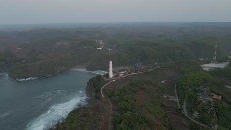 Vista-Aérea-Del-Faro-Blanco-En-La-Costa-Montañosa-En-La-Mañana-Brumosa---Baron-Beach,-Yogyakarta,-Indonesia