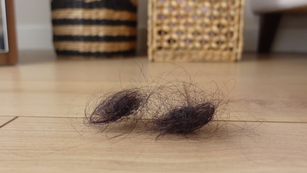 Woman's hand picking up hair from a wooden floor