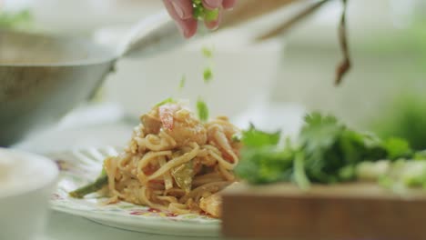 Woman-adding-greens-on-portion-of-wok-noodles