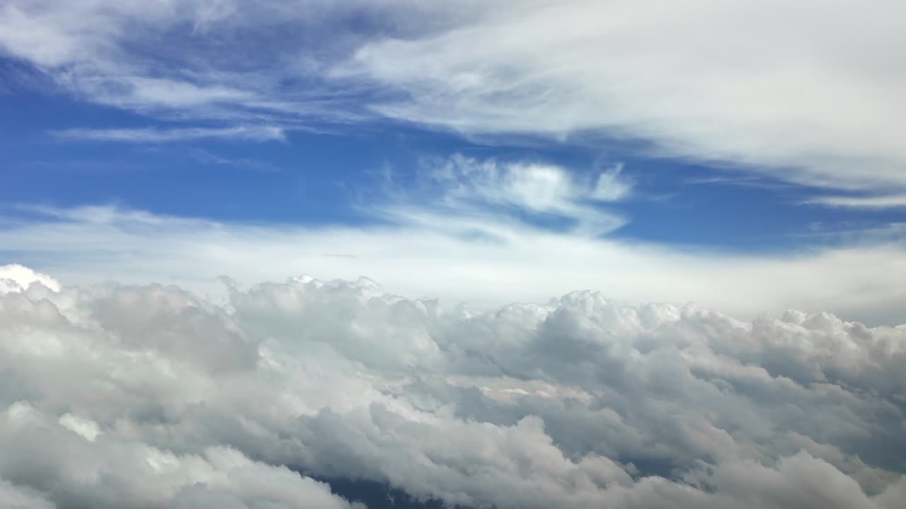 An aerial view taken from inside a jet cockpit while flying through a dreamy cloudscape with cottony and ethreal white clouds with a deep blue sky at the back.
