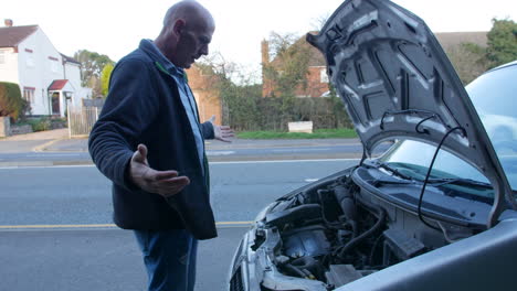 Ein-Frustrierter-Reifer-Mann,-Dessen-Auto-Kaputt-Gegangen-Ist,-öffnet-Die-Motorhaube-Seiner-Motorhaube,-Um-Den-Motor-Zu-überprüfen