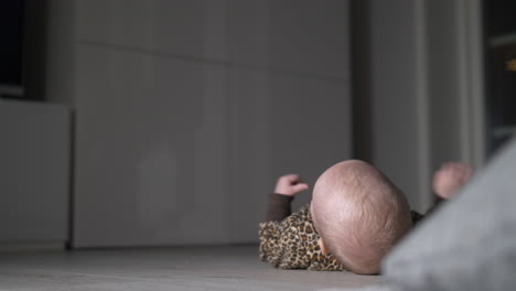 close-up of caucasian baby in leopard jumpsuit rolling over itself on floor